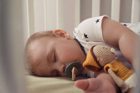Adorable little baby with pacifier and toy sleeping in crib, closeupの写真素材