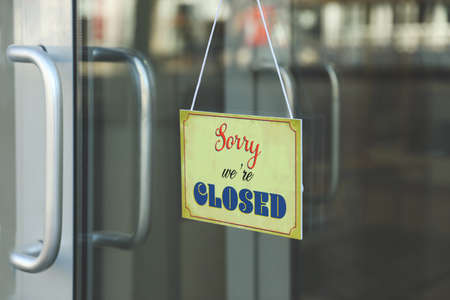 Yellow sign with text Sorry we're Closed hanging on glass door.の写真素材