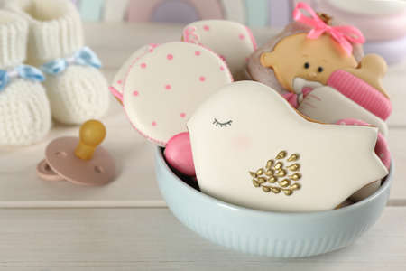 Cute tasty cookies of different shapes, pacifier and booties on white wooden table, closeup. baby...