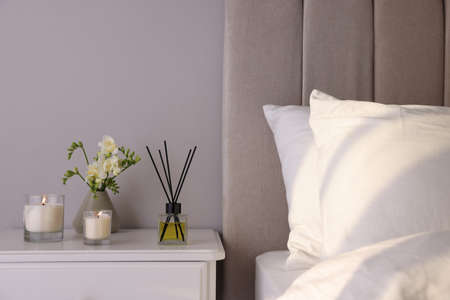 Aromatic reed air freshener, freesia flowers and candles on white bedside table in bedroomの写真素材