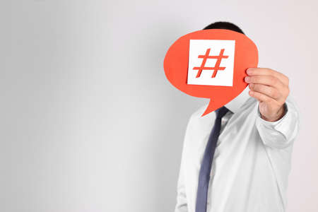 Man holding paper speech bubble with hashtag symbol in front of his face on light background. Space...