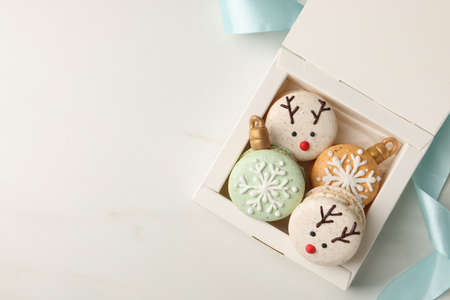 Beautifully decorated Christmas macarons in box and ribbon on white table, flat lay. Space for textの写真素材