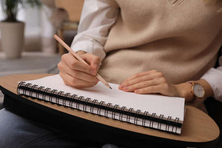 Woman drawing in sketchbook with pencil at home, closeup
