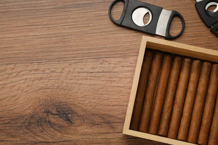 Box with cigars and guillotine cutters on wooden table, flat lay. Space for textの写真素材
