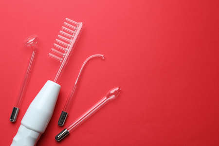 Modern darsonval with nozzles on red background, flat lay. Space for text