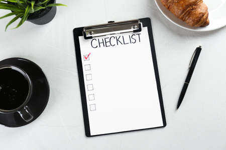 Clipboard with inscription Checklist, cup of coffee and croissant on white table, flat layの写真素材