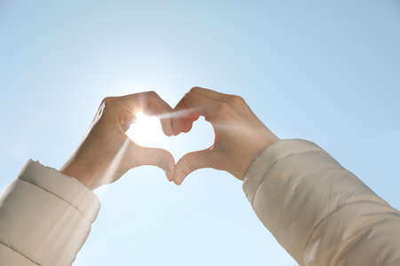 Woman showing heart against blue sky outdoors on sunny day, closeup of hands