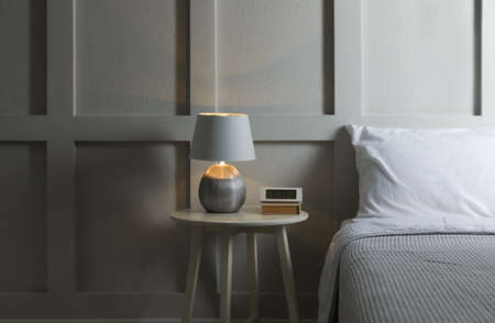 Stylish lamp, alarm clock and book on bedside table indoors. bedroom interior elements