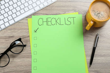 Paper sheet with inscription Checklist, computer keyboard, cup of coffee and eyeglasses on wooden table, flat layの写真素材