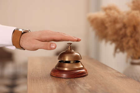 Man ringing service bell at wooden reception desk in hotel, closeupの写真素材