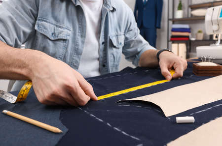 Tailor working with fabric at table in workshop, closeup