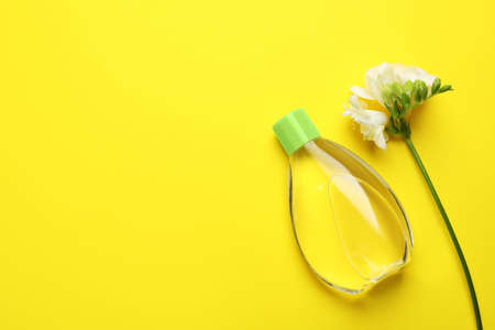 Bottle of baby oil and blooming freesia on yellow background, flat lay. Space for textの写真素材
