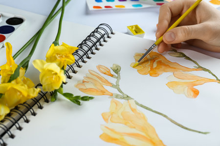 Woman painting freesias in sketchbook at white table, closeupの写真素材