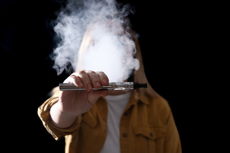 Young woman holding electronic cigarette against black background, focus on handの写真素材