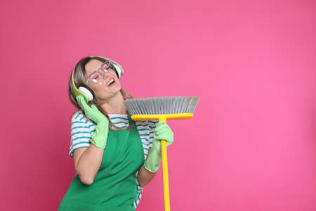 Beautiful young woman with headphones and floor brush singing on pink background. Space for text
