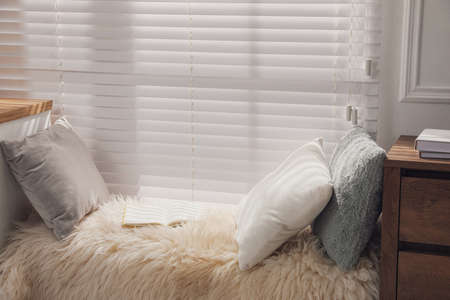 Comfortable place to relax with faux fur and pillows near window in room