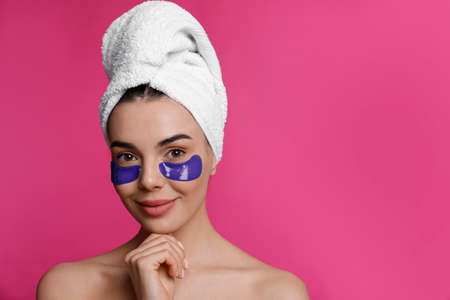 Beautiful young woman with under eye patches and hair wrapped in towel on pink background, space for textの写真素材