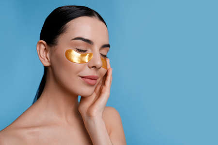 Beautiful young woman with under eye patches on light blue background, space for text