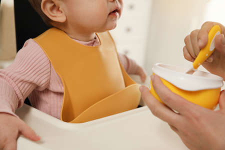Mother feeding her little baby indoors, closeup. Kid wearing silicone bibの写真素材
