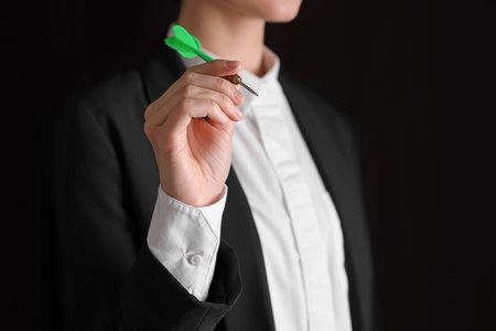 Businesswoman holding green dart on black background, closeupの写真素材