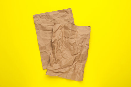 Sheets of crumpled brown paper on yellow background, top viewの写真素材