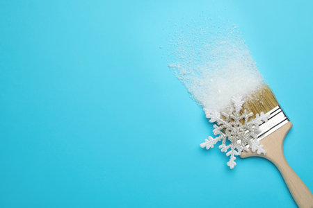 Brush painting with artificial snow on light blue background, top view. Space for text. creative...