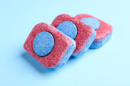 Dishwasher detergent tablets on light blue background, closeup