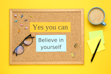 Corkboard with motivational quotes, cup of coffee and office stationery on yellow background, flat layの写真素材