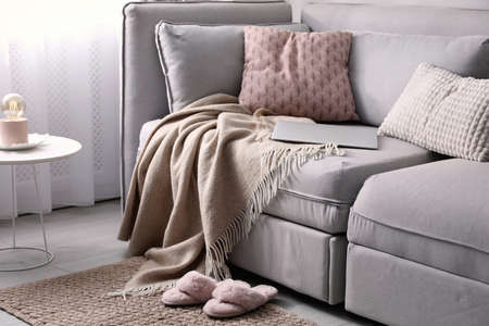Comfortable sofa with pillows, plaid and laptop in living room. interior design