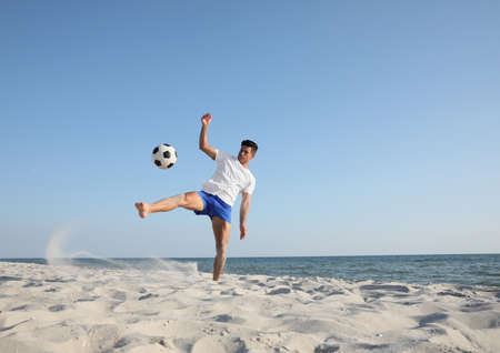 Man kicking football ball on beach near seaの写真素材