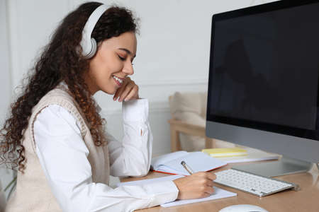 African American woman with headphones using modern computer for studying at home. distance learning