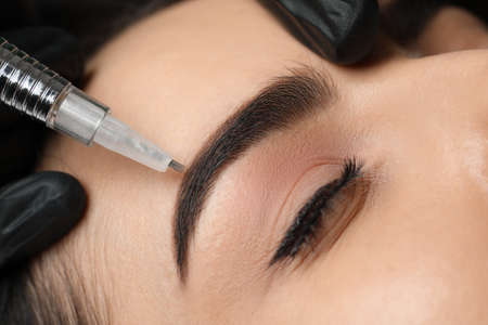 Young woman undergoing procedure of permanent eyebrow makeup in salon, closeup