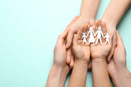 Parents and child holding paper cutout of family on light blue background, top view. Space for textの写真素材
