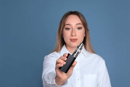 Young woman holding electronic cigarette against light blue background, focus on hand. Space for...