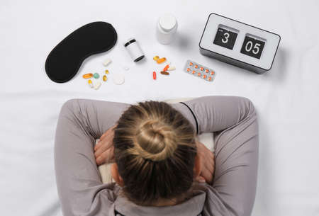 Woman surrounded by different pills on white bedsheet, top view. Insomnia treatment