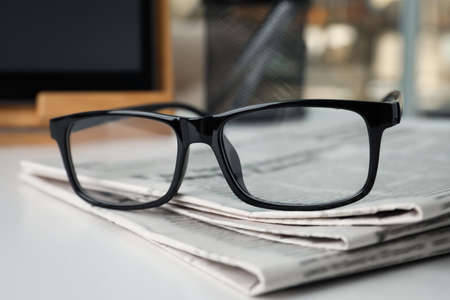 Stack of newspapers and glasses on white table indoors, closeup