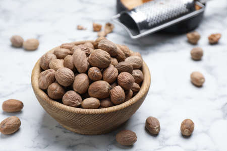 Scattered nutmeg seeds, wooden bowl and grater on white marble tableの写真素材