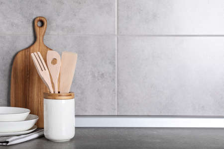 Holder with kitchen utensils, ceramic dishes and cutting board on gray table. Space for text