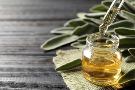 Dropping essential sage oil into bottle on gray wooden table, closeup. Space for textの写真素材