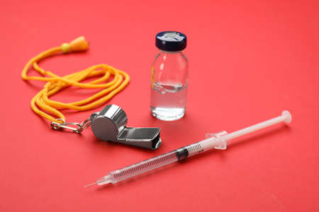 Referee whistle, syringe and vial on red background. Doping conceptの写真素材