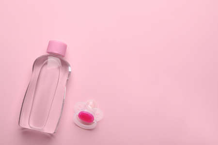 Bottle of baby oil and pacifier on pink background, flat lay. Space for textの写真素材