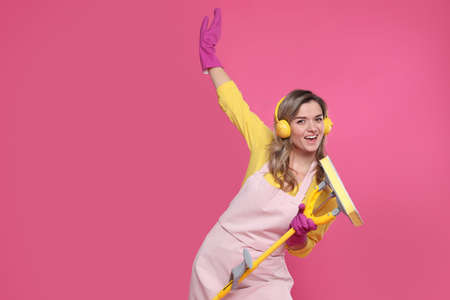 Beautiful young woman with headphones and mop singing on pink background. Space for textの写真素材