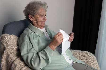 Elderly woman with letter in armchair indoors. Loneliness conceptの写真素材