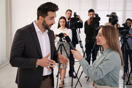 Professional young journalist interviewing businessman and group of video camera operators on backgroundの写真素材