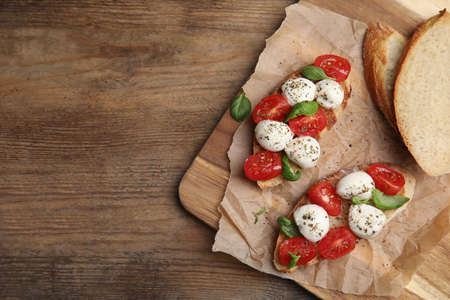 Delicious sandwiches with mozzarella, fresh tomatoes and basil on wooden table, top view. Space for...