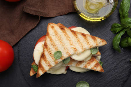 Delicious grilled sandwiches with mozzarella, tomatoes and basil on black table, flat layの写真素材