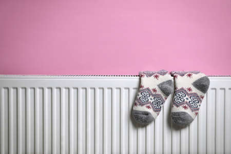 Modern radiator with knitted socks near pink wall indoors, space for textの写真素材