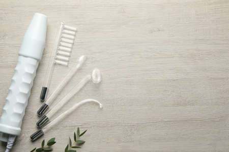 Flat lay composition with darsonval and different nozzles on white wooden table, space for text