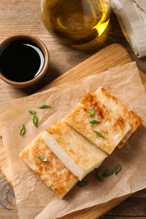 Delicious turnip cake with green onion and soy sauce on wooden table, flat layの写真素材