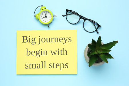 Motivational quote Big journeys begin with small steps, houseplant, glasses and alarm clock on light...